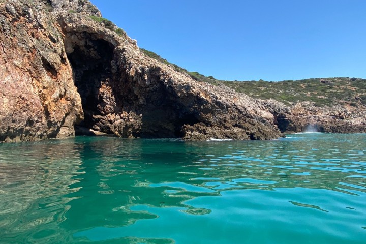 Rocky coastal cave with turquoise water under a clear blue sky.