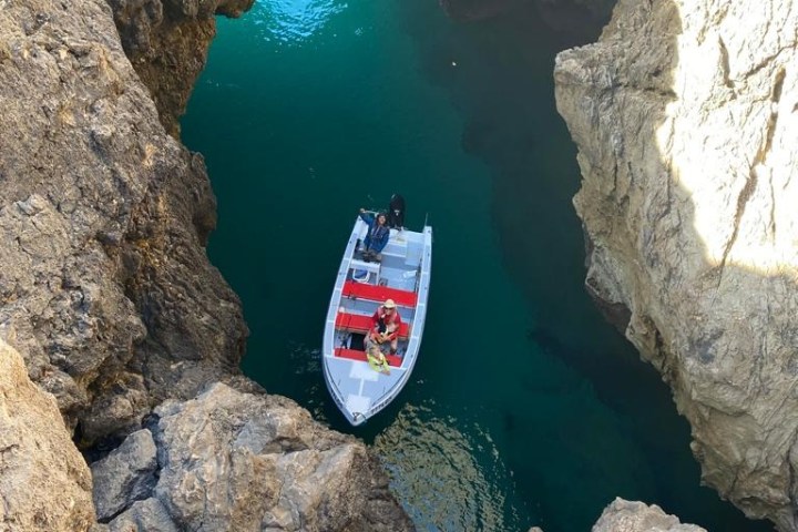 A boat with people navigating through a rocky cave with turquoise water.