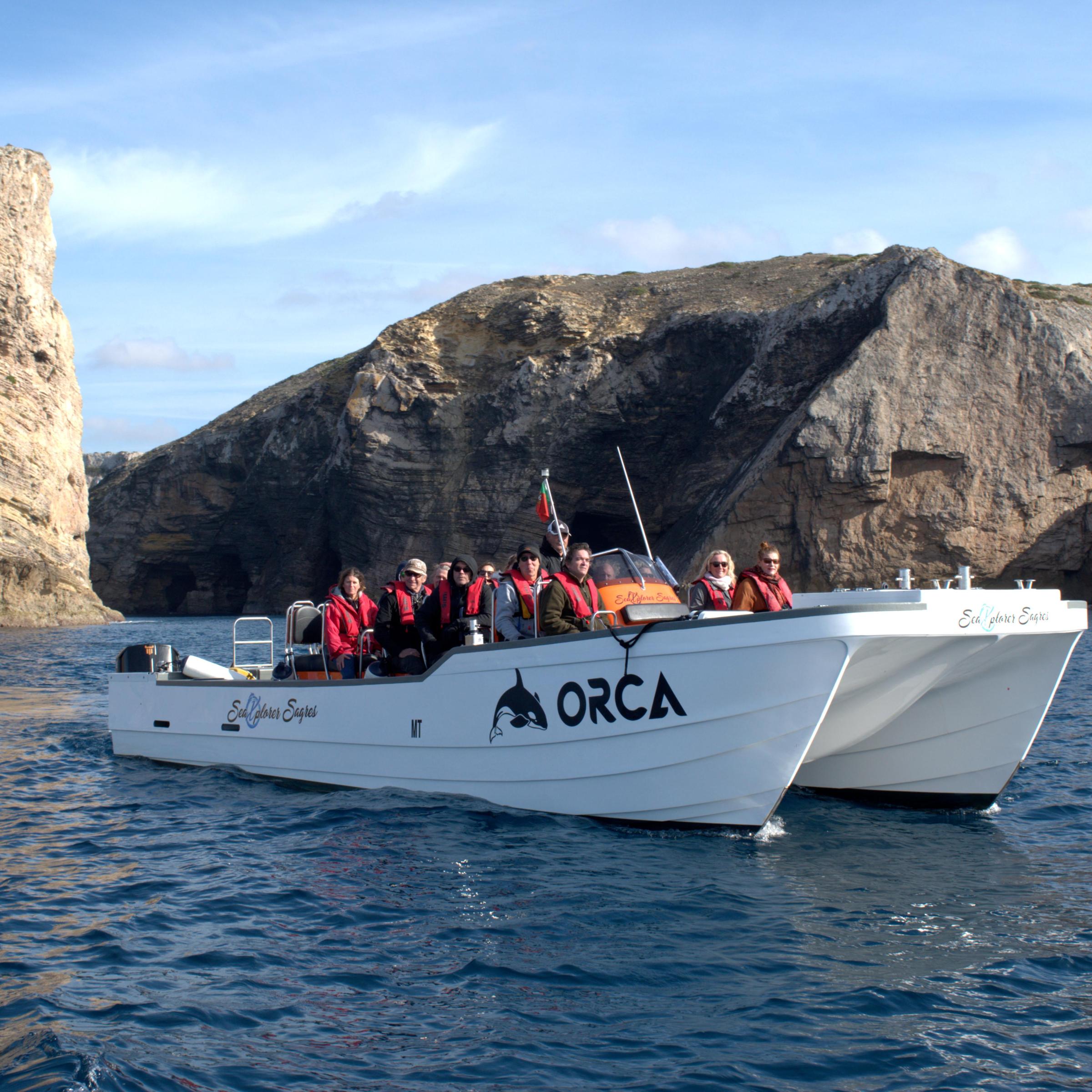 Tourists in red jackets on a white boat near rocky cliffs.
